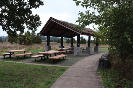 Covered picnic shelter and outdoor picnic tables  on hard surface – near parking lot